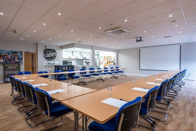 The training room, set up in boardroom style, facing the projector screen. Each place setting is set with writing materials and a glass.